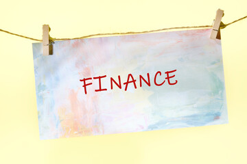 A vibrant piece of paper with the word finance written boldly in red is attached to a line by clothespins