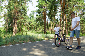 Obraz premium Girl learning to ride a bicycle with her father in forest. Loving daddy teaching his daughter how to ride a bike