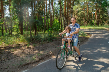 Fototapeta premium A young father carries his little daughter in a bicycle seat. Dad and child ride a bike in forest