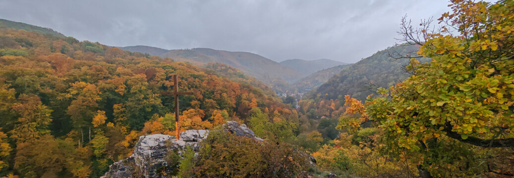 Wide panoramic view from Moln&aacute;r Rock showing the valley of Lillaf&uuml;red surrounded by colorful autumn forest and mountain ridges beneath cloudy sky.