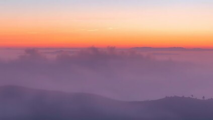 A breathtaking sunrise paints the sky with vibrant orange and purple hues over a misty mountain landscape.