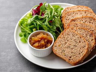 Plate with slices of whole grain bread, fresh green salad, and small bowl of fruit chutney, creating healthy and appetizing