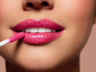 Close up of woman applying pink lip gloss with makeup applicator, showcasing glossy lips and smooth skin
