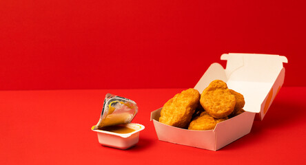 Chicken nuggets in a paper container and yellow dipping sauce. 紙容器に入ったチキンナゲットと黄色のディッピングソース（マスタードソースなど）。	

