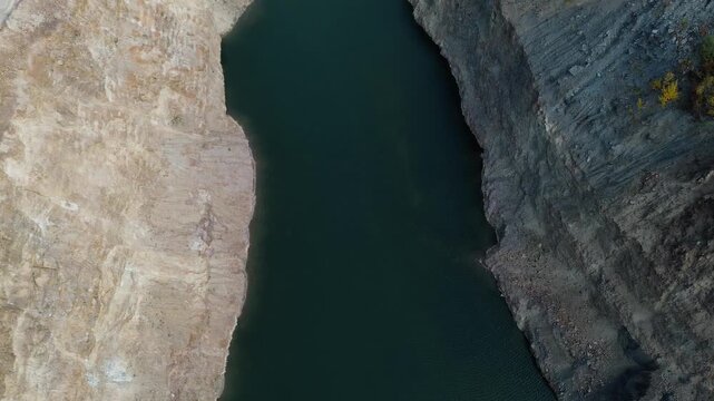 Aerial view of a flooded quarry surrounded by colorful autumn forest in Fruska Gora, Serbia. Calm turquoise water contrasts with rocky cliffs and seasonal foliage. Horizontal 4k footage