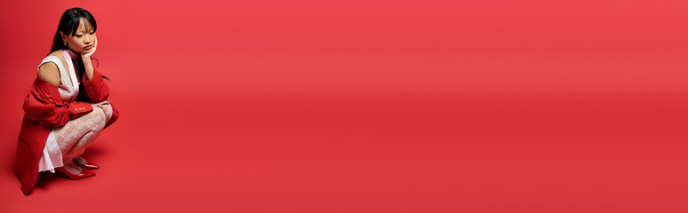 Stylish young woman in red and white attire poses thoughtfully in bold colors