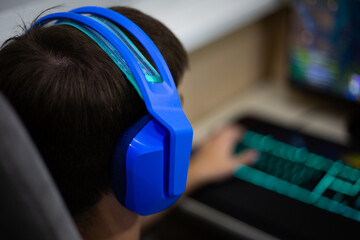 Close up of person wearing blue gaming headphones while playing game on computer. The vibrant colors of the headphones and keyboard highlight the immersive gaming experience