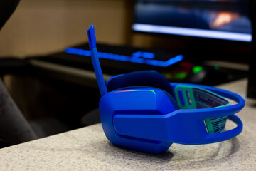 Close up shot of modern, illuminated blue gaming headset resting on table, with vibrant colors reflecting the dynamic and high tech world of gaming and e sports. Computer gaming setup at home