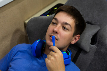 Young gamer has removed his blue gaming headphones but is using microphone to communicate with...