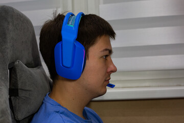 Young man wearing blue gaming headphones, deeply immersed in his gaming session. Image showcases modern technology, emphasizing comfort and style in focused, digital leisure environment