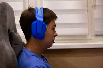 Person wearing bright blue gaming headphones while seated comfortably in chair, engrossed in gaming session. Perfect for projects related to gaming culture, e sports and tech enthusiasts