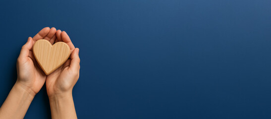 Hands holding wooden heart on blue background, symbolizing charity and care