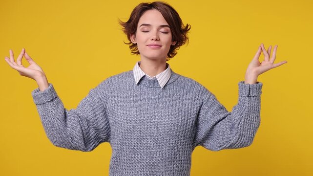 Spiritual tranquil young woman she wear grey knitted sweater white shirt casual clothes hold spreading hands in yoga om aum gesture relax meditate try to calm down isolated on plain yellow background