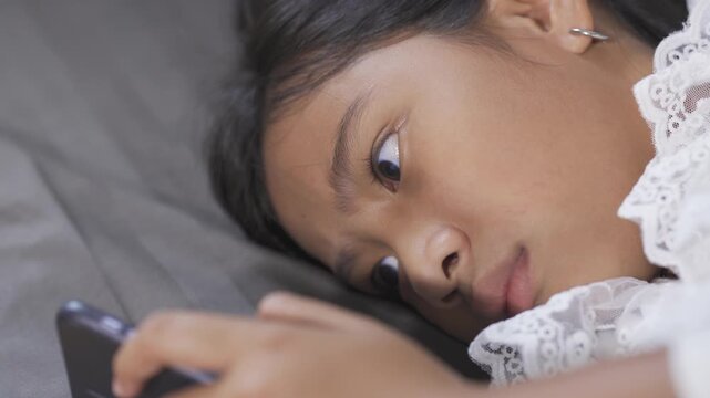A child using smart phone lying in chair  playing games, watching videos online, scrolling screen. Children's screen addiction. 
