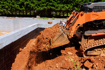 Excavator pouring dirt from ground as construction progresses on building foundation