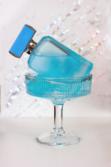 Blue bottle of eau de toilette in a cocktail glass with blue ice on a light background	