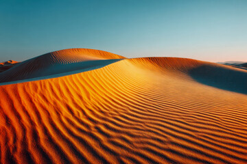 Golden sunlight casting intricate shadows and patterns over rolling desert sand dunes under a clear blue sky at sunset or sunrise hours