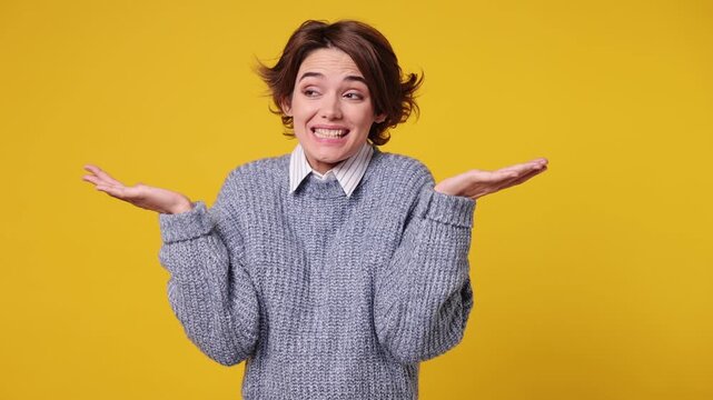 Hesitant indecisive fun shy young woman she wear grey knitted sweater white shirt casual clothes feels doubtful spreading hands say oops ouch oh omg i am so sorry isolated on plain yellow background