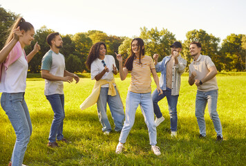 Positive friends dancing and playing together in city park, laughing during leisure party, sharing fun, enjoying group happiness, entertainment, creating joyful vibes in an outdoor setting.