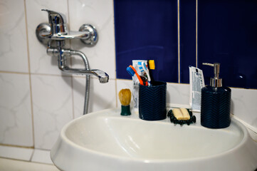 A bathroom sink with a silver faucet, a blue toothbrush holder, a soap dispenser, and various toiletries on the countertop