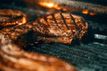Grilled pork chops in flames . A jumbo pork chop placed on a grill with fire in the background.