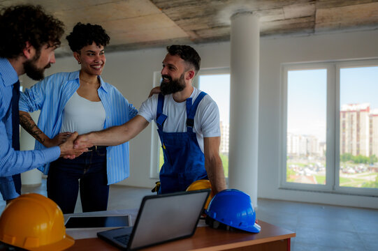 Architects and a construction worker shaking hands inside an unfinished building, celebrating successful collaboration and teamwork in the construction industry