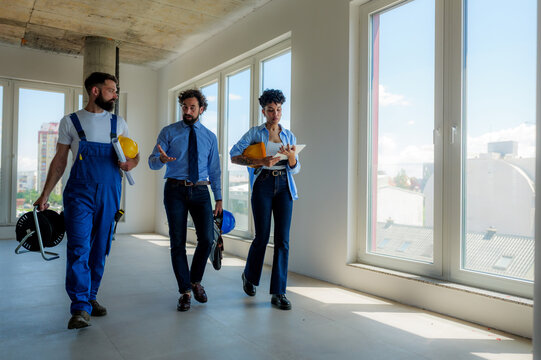 Architects, construction workers, and engineers walking through a construction site, discussing plans and progress while reviewing blueprints and using digital technology