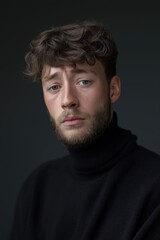 Fototapeta premium Young caucasian male with curly hair in black turtleneck against dark background