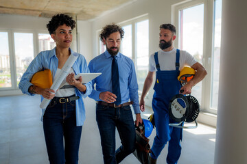 Architect, manager, and electrician walking through a building under construction, discussing plans and blueprints for the project while collaborating on design and development details