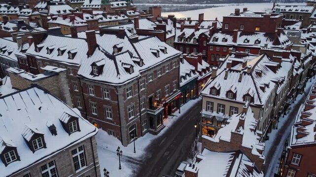Aerial video of a snow-covered European-style town at dusk, showcasing charming rooftops and historic architecture with a serene winter backdrop.