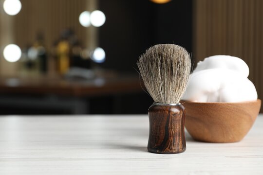 Shaving brush and bowl of foam on light wooden table in barbershop, closeup. Space for text - Powered by Adobe