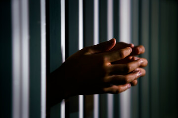 Hands Reaching Through Jail Bars in a Dimly Lit Prison Cell