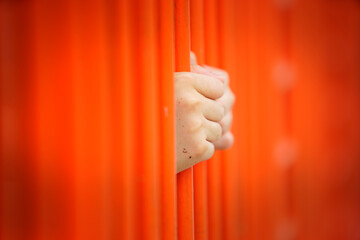 Hands Grasping Orange Bars Behind a Prison Cell in Soft Focus