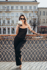 Stylish woman in black jumpsuit posing on city balcony