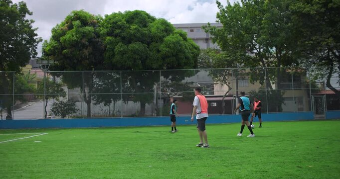 Group of friends playing casual soccer on neighborhood field, wearing orange and blue vests, enjoying friendly match and teamwork in relaxed community environment