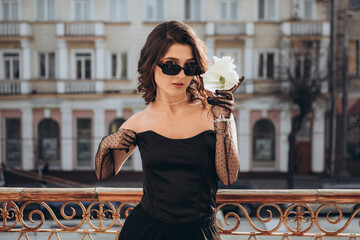 Glamorous woman holding white flower on city balcony