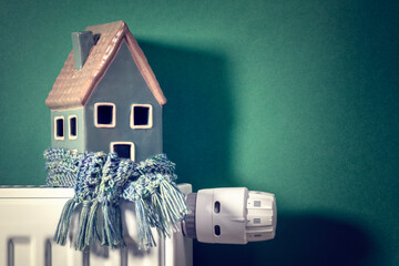 House model wrapped in green scarf on radiator winter energy, heating and insulation background