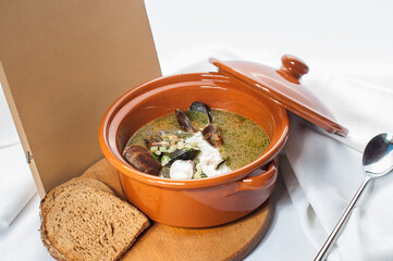 Mussel soup in a clay pot on a wooden board on a white background