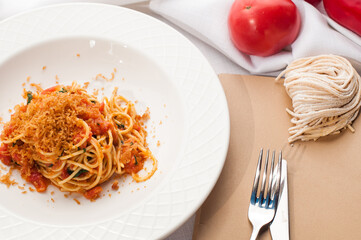 Italian pasta with tomatoes and herbs in a white plate on a table in a restaurant