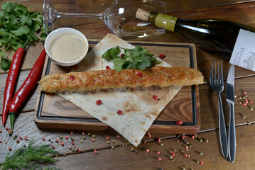 large kebab on a wooden board with pita bread and herbs