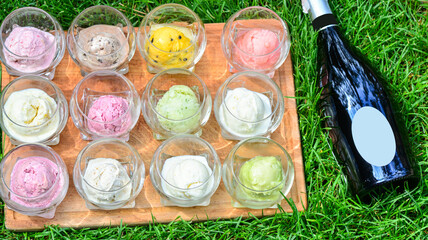 different types of ice cream in cups on a wooden board on the grass with a prosecco bottle