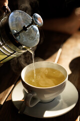 A close-up image of hot tea being poured from a French press into a white cup.