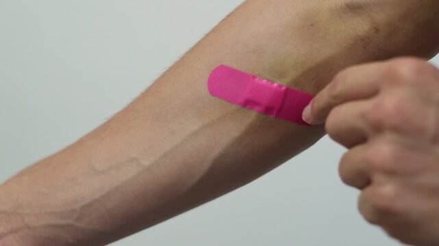 removing pink bandage from forearm &mdash; first aid