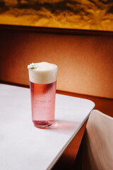 Refreshing pink drink served in a clear glass with foam and a flower garnish