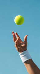 Energetic male hand tossing yellow tennis ball, clear blue sky