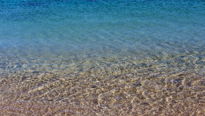 Transparent shallow sea water over a sandy seabed reflecting sunlight in gentle ripples.