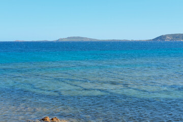 Wide view of a blue sea with varying shades of turquoise and islands on the horizon under a clear sky.