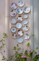 Decorative wall with vintage floral porcelain saucers arranged artistically beside blooming pink flowers.