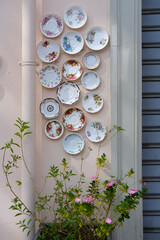 Artistic wall decoration made of vintage floral porcelain saucers arranged above blooming pink flowers.