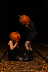 Two figures with pumpkin heads sitting on train tracks during autumn night in a spooky scene